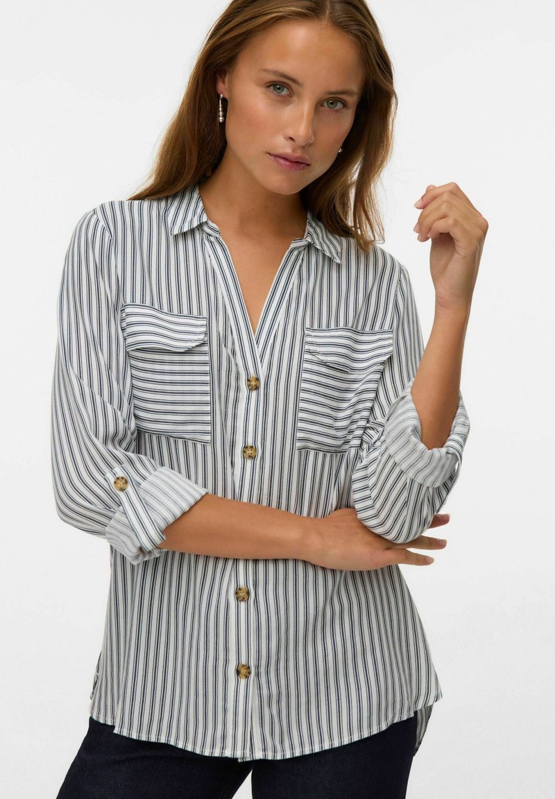 Chemise à rayures en tissu léger, dotée de deux poches poitrine, de manches roulées et de boutons contrastants. La palette de couleurs est blanche et marine.
