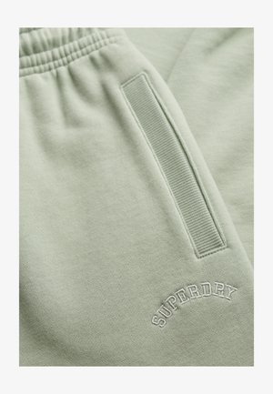 Lichtgroene sweatpants van zacht materiaal, met een ribbelzijdige zak en geborduurd "SUPERDRY" logo in het wit.