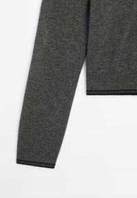 Manche de pull en tricot gris avec un poignet en côtes et des rayures d'accent foncé le long du bord. Le tissu semble doux avec une texture lisse.