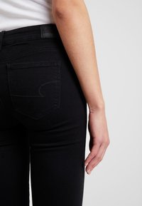 Svart denim jeans med middels høyde, subtil søm på baklommene og en jevn, elastisk tekstur for komfort.
