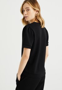 Zwart T-shirt met korte mouwen en een ronde hals, voorzien van pofmouwen en een relaxte pasvorm. Glad textuur met een effen kleur ontwerp.
