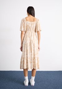 Blomsterdekorert beige maxi-kjole med korte puff-ermer, elastisk liv og lagdelt kant; parret med hvite sneakers og ankelsokker.