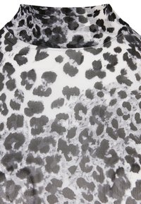 Tkanina sa uzorkom leoparda ima visoki izrez, sa motivom crnih i sivih tačaka na beloj pozadini. Materijal deluje lagano i prozračno.