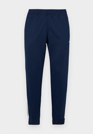 Donkerblauwe sportbroek met een elastische tailleband, taps toelopende pijpen en witte strepen aan de zijkant die verticaal lopen. Soepele stoftextuur.