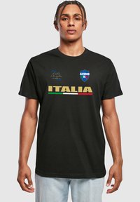 Sort bomulds T-shirt med teksten "ITALIA" i guld, grøn og rød. Inkluderer dekorative logoer og tekst i blå og hvid på brystet.