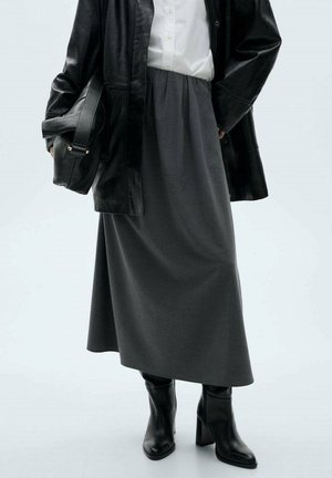 Persoon met een zwarte leren jas, wit shirt, grijze midi-rok, zwarte laarzen met hak, en een zwarte leren handtas vasthoudend.