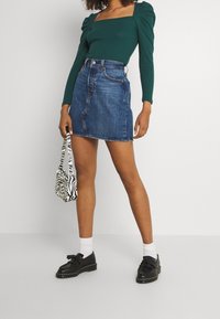 Grön långärmad topp med fyrkantig halsringning, puffärmar; blå denim minikjol; zebramönstrad väska; svarta skor med vita strumpor.