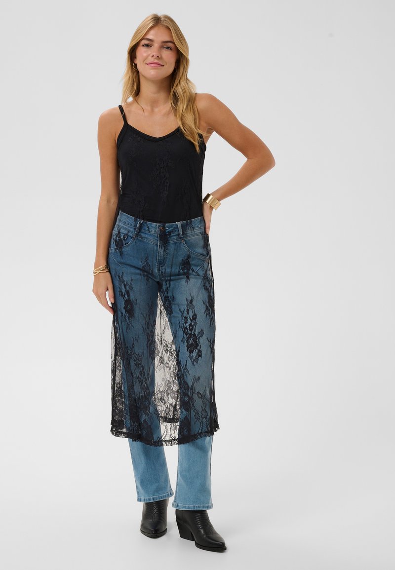 Schwarzes Spitzenoberteil über blauen Jeans, mit einem durchsichtigen Spitzen-Overlay mit Blumenmuster, verstellbaren Trägern und einem geraden Bein-Design mit Stiefeln.