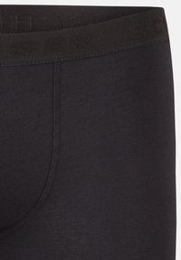 Boxers en tissu extensible noir avec une large ceinture texturée en relief et une texture lisse, avec des détails de couture minimaux.