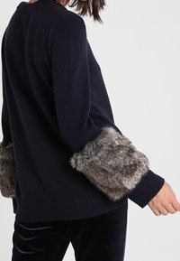 Maglione navy con polsini in finta pelliccia texturizzata. Presenta un collo a costine, una vestibilità ampia e un tessuto in maglia morbido. Design semplice e moderno.