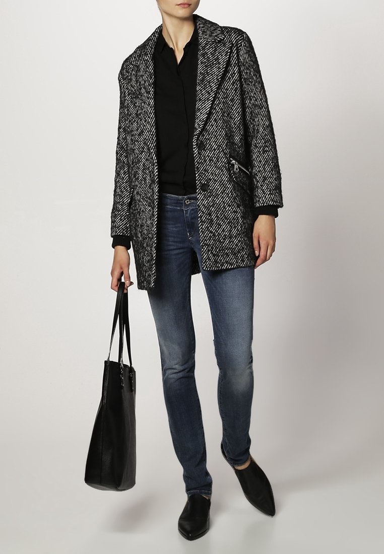 Abrigo de gran tamaño en blanco y negro con estampado de pata de gallo, camisa negra, vaqueros azules, bolso tote negro y zapatos negros de punta.