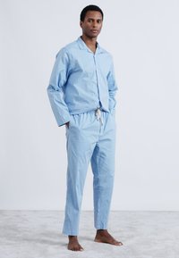 Svetlo modra bombažna pižama z ovratnikom in zapenjanjem na gumbe ter hlačami z elastičnim pasom, ki imajo detajl z vrvico in gladko teksturo.