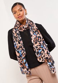 Šála s leopardím potiskem v odstínech oranžové, černé a modré, vyrobená z lehké texturované látky, volně přehodena kolem krku.