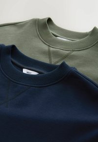 Deux sweat-shirts à col rond pliés, un bleu marine et un vert olive, avec des cols côtelés et des détails de couture visibles.