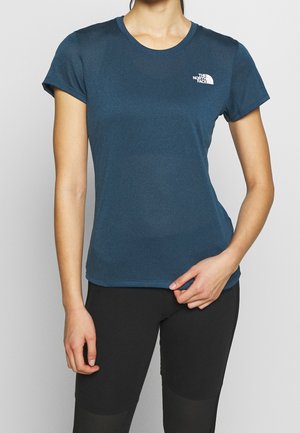 Kobieta ubrana w dopasowaną ciemnoniebieską koszulkę z krótkim rękawem z logo The North Face i czarne legginsy sportowe na jednolitym tle.