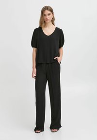 Čierny dvojdielny outfit pozostávajúci z voľného, krátkeho rukávu s výstrihom do V a širokých nohavíc. Hladká, ľahká tkanina s jemným splývaním.