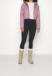 Ljuslila kort jacka med huva, svarta leggings och tanmocka ankle boots med ribbad kant. Slät textur och modern passform.