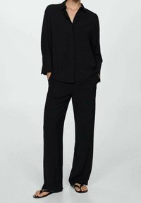 Chemise noire ample avec col et boutons sur le devant, associée à un pantalon large assorti. Texture douce, design minimaliste et coupe décontractée.