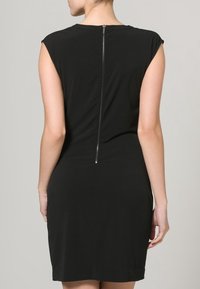 Černé šaty s krátkými rukávy, přiléhavým střihem a decentním kovovým zipem na zadní straně pro zapínání. Hladká, elastická látka.