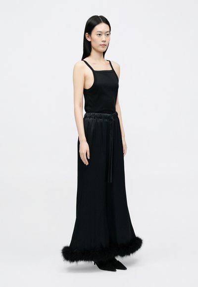 Crni top bez rukava s četvrtastim izrezom uparен s crnim širokim hlačama s krznom na rubu. Glatki materijal, ležeran kroj.