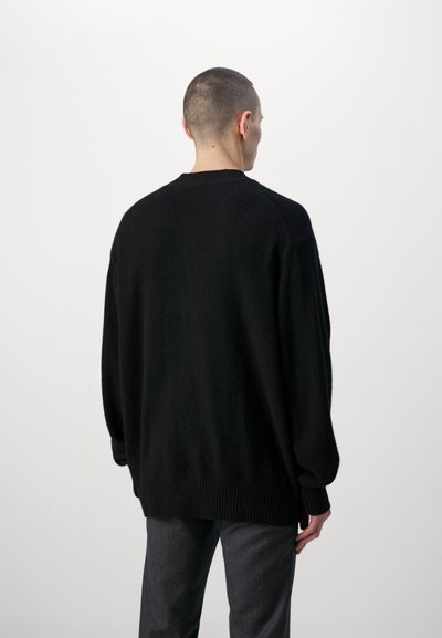 Jersey negro de gran tamaño con escote redondo, puños y dobladillo acanalados, hecho de un material de textura suave. La vista trasera muestra un ajuste relajado.