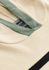 Cremefarbener Hoodie mit einem grünen, strukturierten Kragen. Verfügt über einen schwarzen Streifen am Saum und ein Etikett mit der Marke „NEXT“. Aus weichem Stoff, lässiges Design.