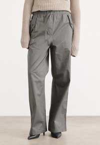 Grijze, losse broek met een elastische tailleband, zijzakken en een gladde textuur, gecombineerd met zwarte puntige hakken.