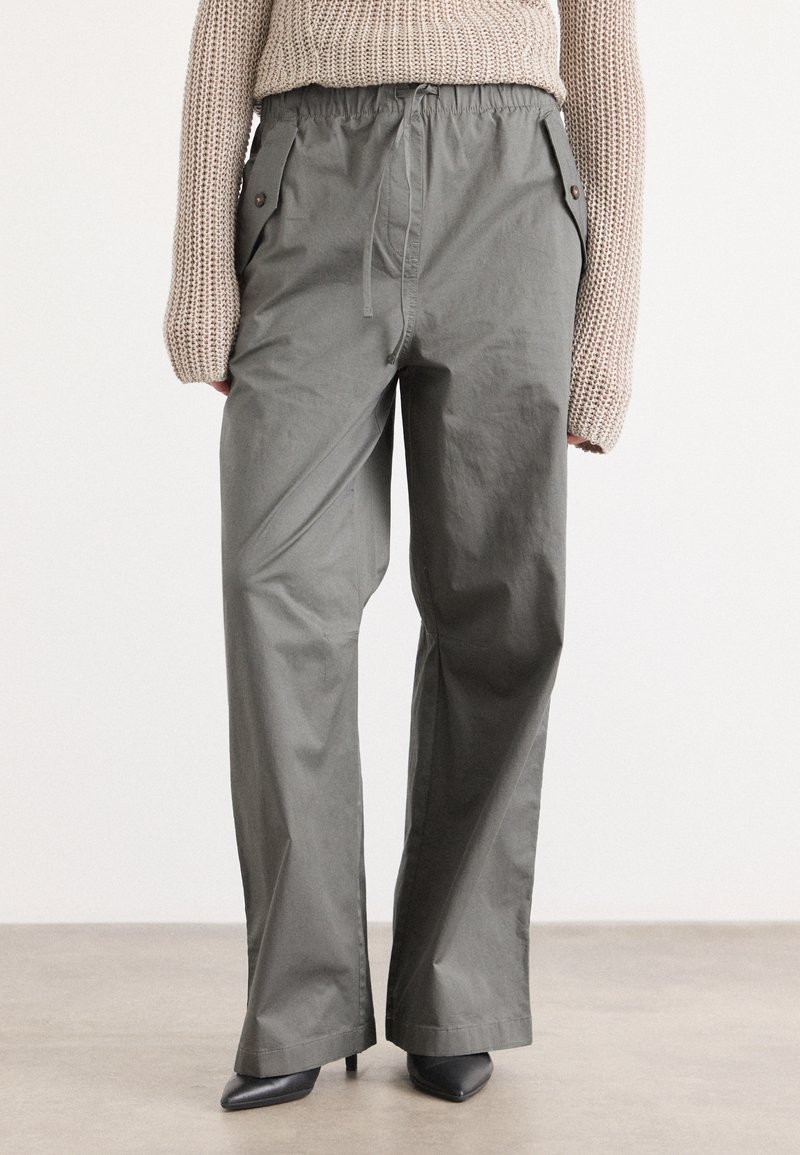 Grijze, losse broek met een elastische tailleband, zijzakken en een gladde textuur, gecombineerd met zwarte puntige hakken.