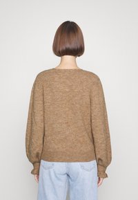 Maglione marrone a costine con un fit rilassato, spalle scese e lunghe maniche a palloncino, abbinato a jeans blu chiaro.