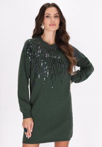 Grünes Strickkleid mit rundem Ausschnitt, langen Ärmeln und einem dekorativen Paillettenmuster in vertikalen Linien auf der Vorderseite.