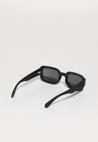 Ochelari de soare negri, rectangulari, cu lentile întunecate, cadru din plastic rezistent și brațe late. Prezintă branding subtil pe tâmplă.