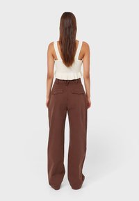 Brown wide-leg pants with two back pockets, paired with a knitted cream top featuring a ribbed texture and a peplum hem.