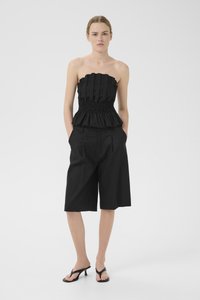 Svart strapless topp med plissert design, smocket midje, kombinert med løse svarte shorts til kneet og svarte flip-flops.