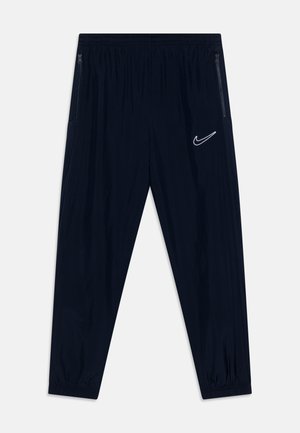 Pantaloni sportivi navy con cintura elasticizzata, gambe affusolate, due tasche laterali con zip e un logo Nike bianco sulla coscia sinistra.