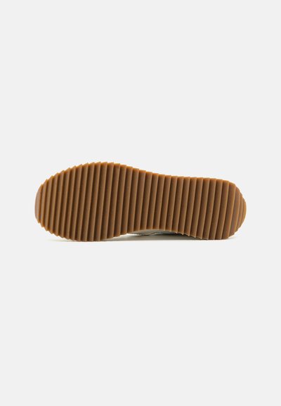 Rubber sole with a wavy texture and pronounced ridges in light brown. The sole features a smooth design with rounded edges.