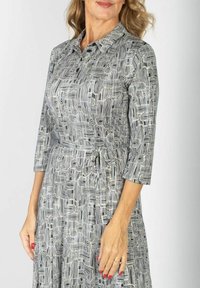 Sukienka z kołnierzykiem w czerni i bieli z abstrakcyjnym wzorem liniowym, rękawy o długości trzech czwartych, pasek w talii oraz miękka tekstura materiału.