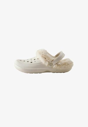 Weißer Slip-On-Clog mit Belüftungslöchern, einem flauschigen beigen Pelzfutter und einem verstellbaren Riemen an der Ferse.