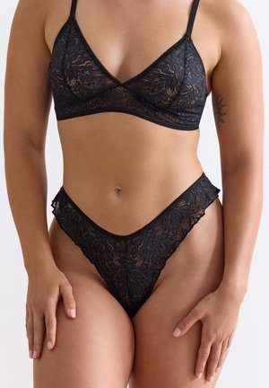 Zwart kanten lingeriesetje bestaande uit een driehoekige bralette en een hooggesneden tanga. Beide stukken hebben bloemmotieven en golvende randen.