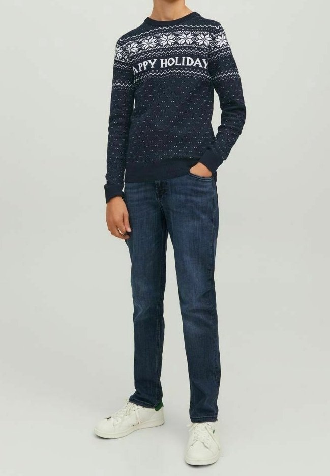 Námořnický svetr s bílým vánočním vzorem a nápisem "ŠŤASTNÉ VÁNOCE", pořízený k tmavým džínům a bílým teniskám se zelenými akcenty.