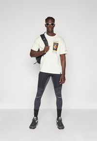 Lys cremefarvet grafisk t-shirt med et Nature's Geographic print, parret med sorte træningsleggings med strukturerede detaljer. Sort rygsæk og sko.