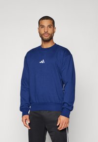 Mörkblå sweatshirt med rund hals och ribbade muddar. Har en liten vit Adidas-logotyp på bröstet. Mjuk tyg med en avslappnad passform.