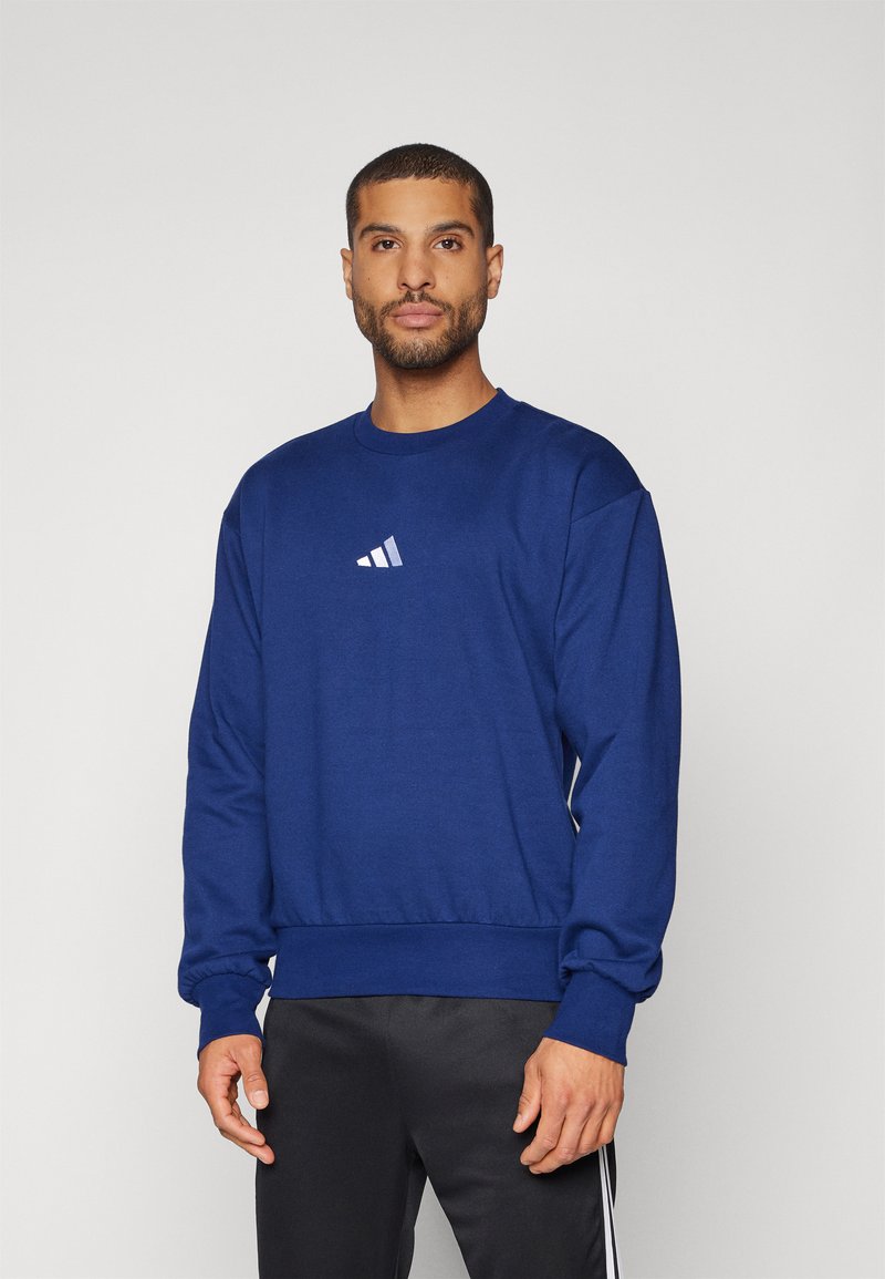 Mörkblå sweatshirt med rund hals och ribbade muddar. Har en liten vit Adidas-logotyp på bröstet. Mjuk tyg med en avslappnad passform.