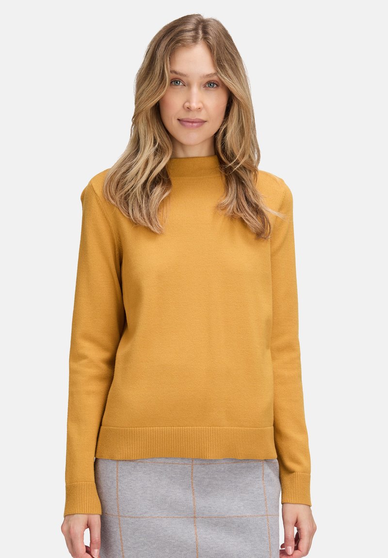 Mustár sárga, hosszú ujjú pulóver bordázott nyakkivágással és mandzsettákkal, sima tapintású és laza fazonú, szürke mintás szoknyával párosítva.