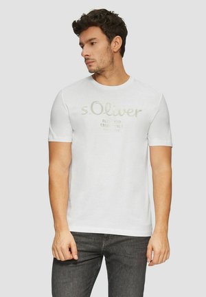 Weißes Baumwoll-T-Shirt mit rundem Halsausschnitt und kurzen Ärmeln, mit einem hellgrauen aufgedruckten Logo auf der Vorderseite. Getragen mit dunklen Jeans.