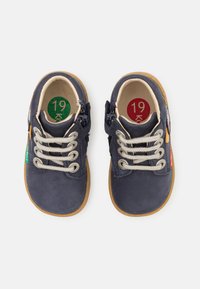 Chaussures en cuir bleu marine avec des lacets gris et des semelles en gomme. Elles sont dotées de fermetures éclair sur le côté et d'inserts colorés avec des indications de taille.