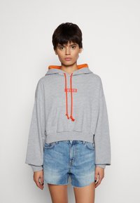 Felpa grigia corta con dettagli arancioni, dotata di tasca frontale e coulisse. Abbinata a pantaloni shorts di jeans a vita alta.
