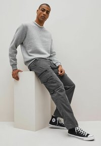 Gray sweatshirt with a crew neckline, paired with cargo pants featuring multiple pockets, and black high-top sneakers with white soles.