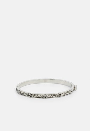 Bransoletka typu bangle w srebrnym odcieniu z kryształowymi zdobieniami i okrągłymi akcentami z logo równomiernie rozmieszczonymi na opasce na białym tle.