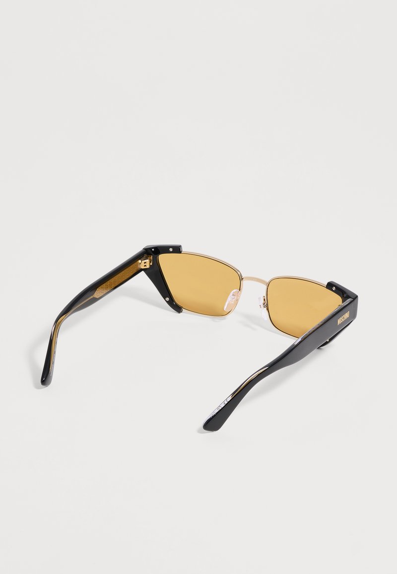 Black-framed sunglasses with gold-tinted rectangular lenses and gold accents resting open on a white surface.