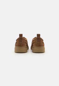 Brown suede shoes with a low profile, featuring a round toe, contrasting rubber sole, and textured back pull tab. Smooth inner lining.